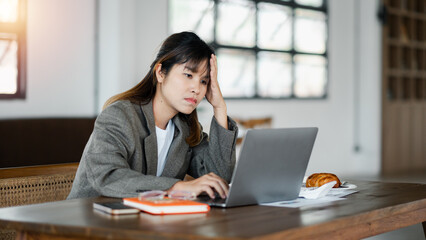 Woman seated at a cafe table, expressing concern while looking at her laptop screen, with hand on forehead.