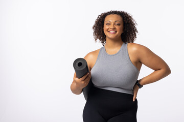 A biracial young female plus size model holding a yoga mat, standing confidently on white background - 788840026