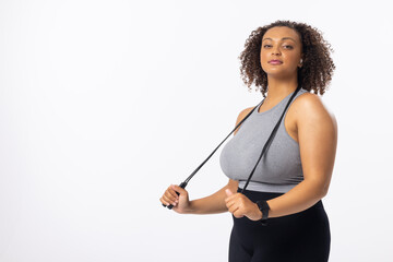 Biracial young female plus size model holding resistance band, looking confident on white background - 788840030