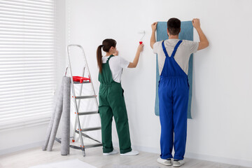 Workers hanging light blue wallpaper in room