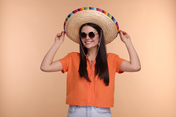 Young woman in Mexican sombrero hat and sunglasses on beige background