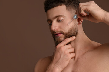 Obraz premium Handsome man applying serum onto his face on brown background, space for text