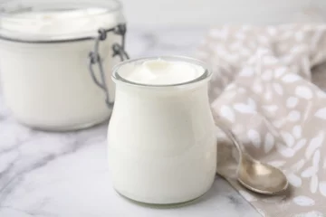 Fotobehang Delicious natural yogurt in glass jars and spoon on white marble table, closeup © New Africa