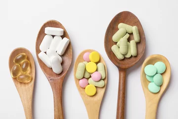 Fotobehang Different vitamin pills in wooden spoons on white background, flat lay © New Africa