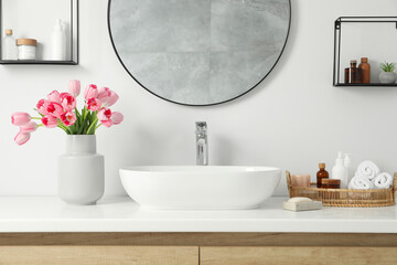 Vase with beautiful pink tulips and toiletries near sink in bathroom