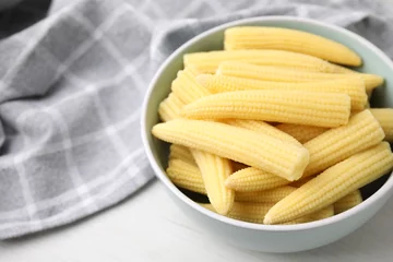 Gordijnen Tasty fresh yellow baby corns in bowl on white wooden table, closeup. Space for text © New Africa
