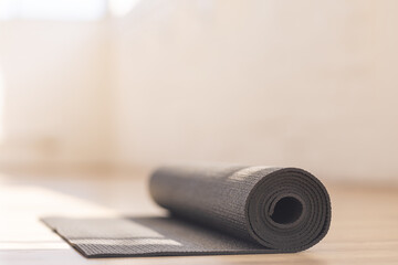 Rolled up yoga mat rests on wooden floor in bright room, copy space