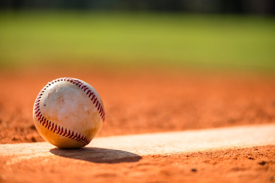 Worn baseball on Pitcher's Mound with dirt and grass in background - Powered by Adobe