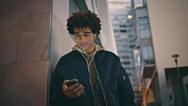Zoomer texting mobile phone lit by city night ambiance closeup. Hispanic guy