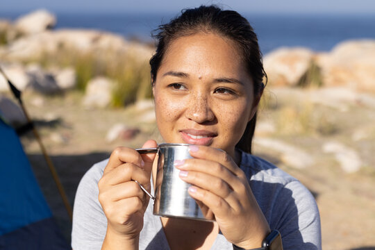 Biracial female hiker holding cup, enjoying a break with adventure nature