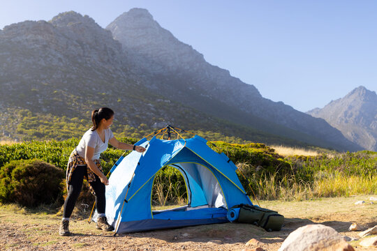 Biracial female hiker setting up tent in mountains, copy space