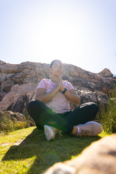 Biracial female hiker sitting cross-legged, hands together, meditating, copy space