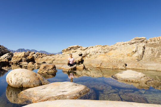 Biracial female hiker sits on rock, reflects in water, copy space