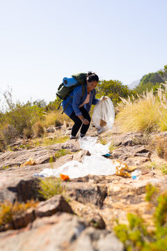 Biracial female hiker collecting trash on mountain trail adventure in nature