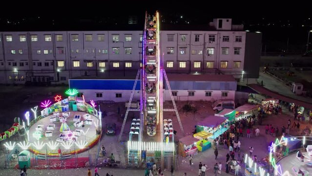 spinning giant wheel close up  to wide pull back drone shot at exhibition in suraram, hyderabad, telangana, india. 4k night time