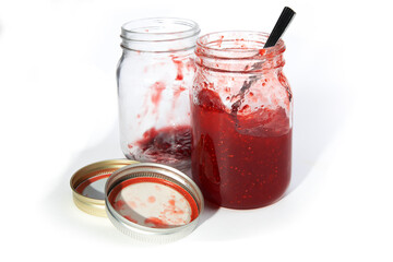 a mason jar full of homemade strawberry jam and a mason jar empty with lids isolated on white