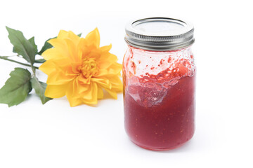 A mason jar of homemade strawberry jam with a yellow flower
