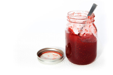 a mason jar of homemade strawberry jam with with its lid open isolated on white