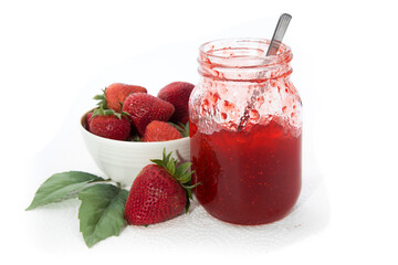 a mason jar of homemade strawberry jam with a bowl full of strawberries isolated on white