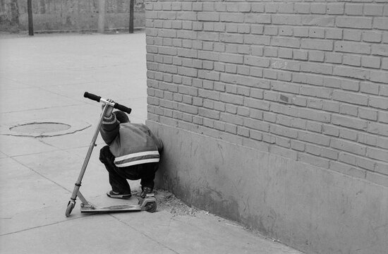 A boy with a scooter peers around a corner at his friends in Beijing, China