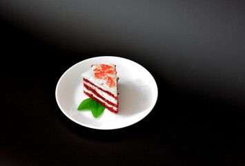 Plate with a piece of cheesecake Red velvet with mint on a black background.