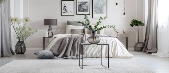 A metal table holds a vase in a large bedroom with a white carpet, a grey lamp, and a gallery on the wall above the bed.