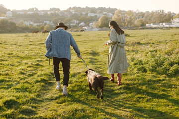 Stylish couple walking with a brown labrador on a nature