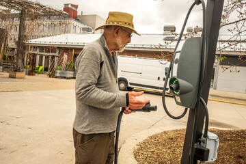 EV charging station: a man ( senior, hat beard and sunglasses) trying to figure out how to use an...