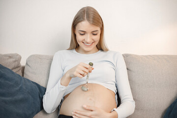 Pregnant lady sitting on a sofa in living room holding a face massager