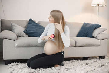 Pregnant lady sitting near a sofa in living room and brushing her hair