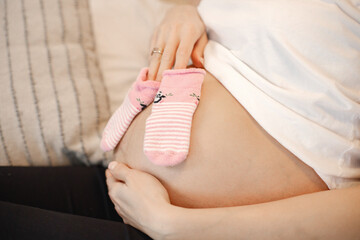 Midsection of pregnant lady lie on a bed and holding a little baby socks