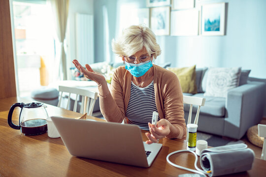 Senior woman with face mask using laptop and feeling unwell at home