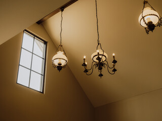 Vintage iron chandelier under the gable roof in the ancient house, Classic style vintage light lamp or candle bulbs hanging at ceiling, indoor, interior loft style building. Retro lighting decoration.