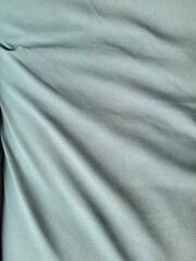 Fototapeta premium Abstract close-up of a mint-colored fabric. The folds on the fabric cast a shadow and create a volumetric background. 