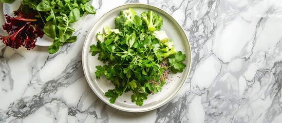 Fresh greens, vegetables, and grains on a light grey marble kitchen counter with a white ceramic plate in the middle. Viewed from above with space for text. Concept of healthy eating, veganism, detox,