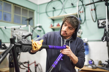 Hispanic young man working on a custom bike frame painting design in purple and black, a creative...