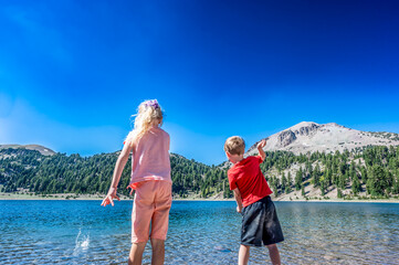 Children throwing rocks from the water's edge of Helen Lake in Lassen Volcanic National Park, California.  - obrazy, fototapety, plakaty