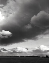 Clouds, very dramatic sky, in black and white. Grainy traditional analog style photo in ultra high resolution. Sunlight is pouting through the silhouette of the cloud formation. Moody, dark.