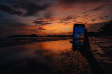 Smartphone takes photos of the calm beach and sky at In the evening at Ao Nang, Krabi.
