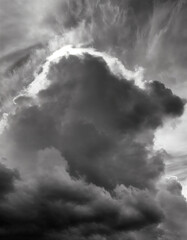 Obraz premium Clouds, very dramatic sky, in black and white. Grainy traditional analog style photo in ultra high resolution. Sunlight is pouting through the silhouette of the cloud formation. Moody, dark.