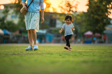 happy toddler girl running with her mother on grass field in park at sunset