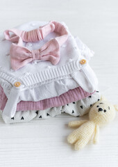 Stack of baby clothes, pink headband and knitted toy bunny.