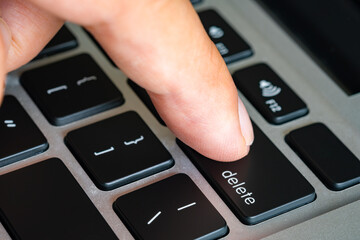 Finger of the computer user, he presses the delete button on the computer keyboard.	