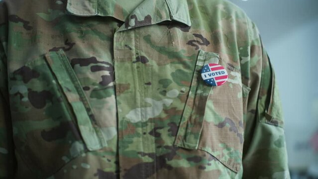 Close up of military man putting on badge with American flag logo and inscription I Voted. US citizen, voter at polling station during elections. National Election Day in the United States of America.