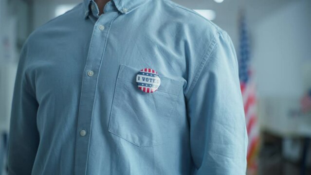 Anonymous Caucasian male voter or businessman puts on badge with American flag logo and inscription I Voted. US citizen at polling station during elections. National Election Day in the United States.