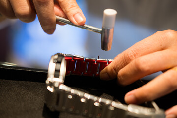 A watch pin being installed into the watch band with a hammer and a watch band holder. Close up