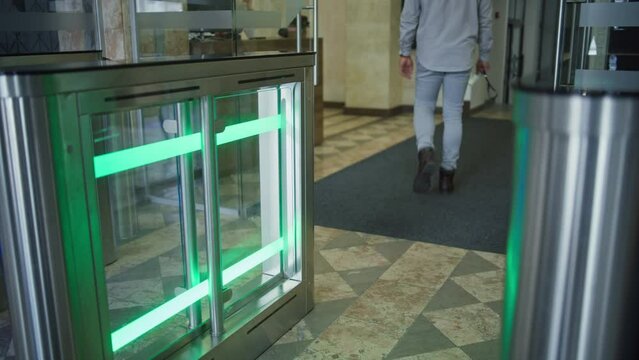 Turnstile with touch panel for automatic scanning and identification in modern office building. Male worker or businessman walks through the gates into business center using electronic pass card.