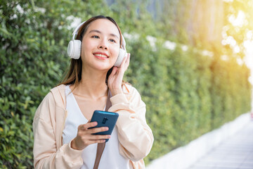 In midst of an urban city garden a happy young woman uses wireless headphones to choose and enjoy her favorite music dancing with pure joy. Her carefree spirit is a beautiful reflection of season.