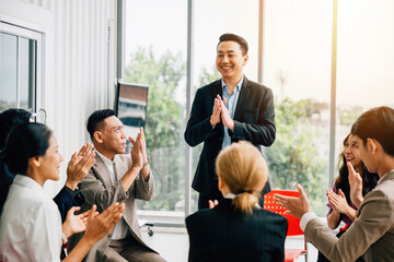 In a meeting, a male speaker shares expertise with the diverse audience. Participants actively raise their hands, asking questions and exemplifying teamwork, learning, and support.