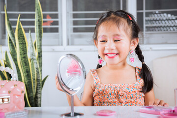 Happy kid is beautiful make up with cosmetics toy, Asian adorable funny little girl making makeup her face she looking in the mirror and applying red lipstick to mouth, Learning activity to be woman